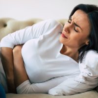 Dysmenorrhea. Close-up photo of a woman, who is lying on her sofa and holding her stomach with suffering facial expression.